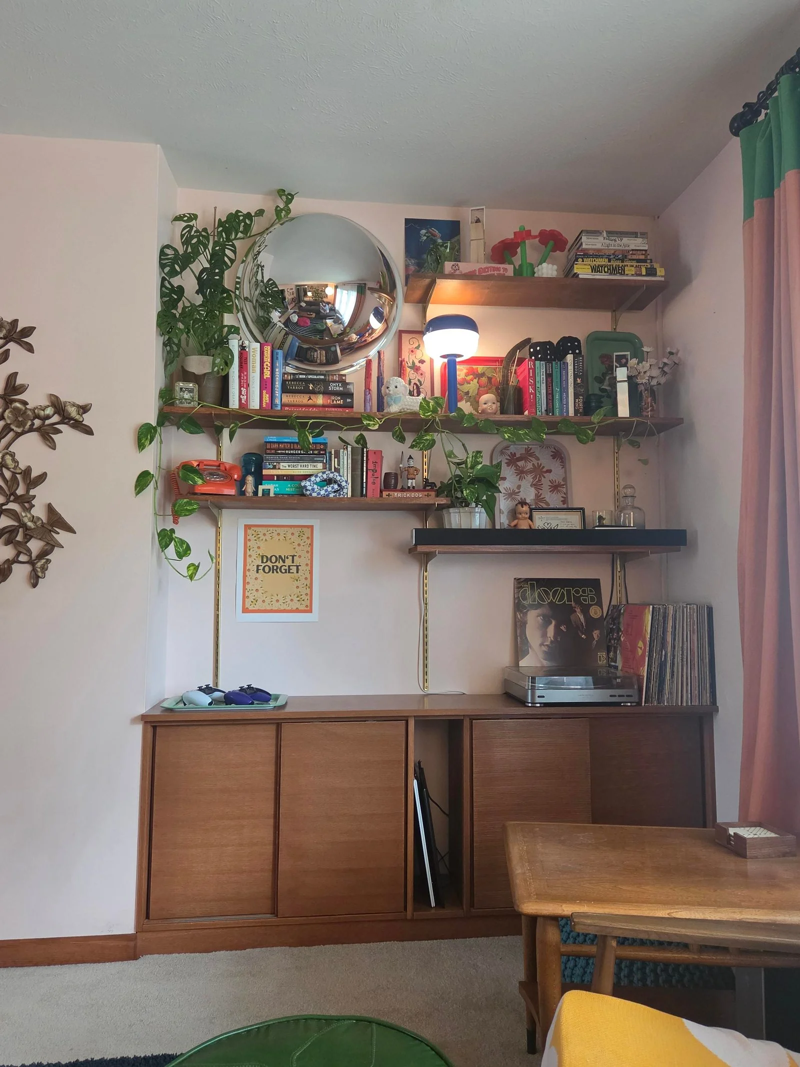Nicchia con mobile basso in legno, giradischi, vinili, mensole con libri, piante e specchio convesso
