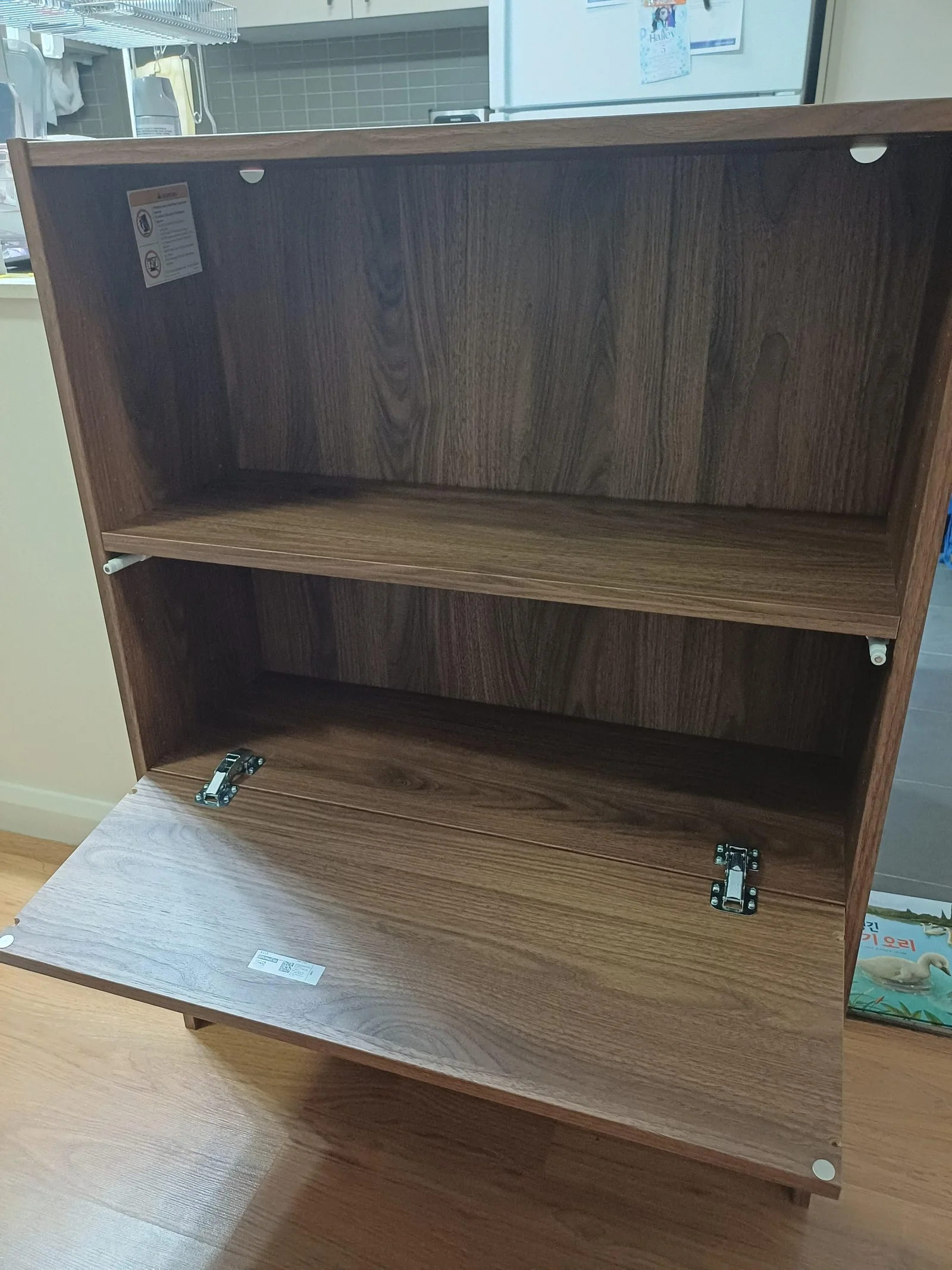 Stessa libreria con l’anta a ribalta aperta: ripiano interno visibile e cerniere metalliche avvitate sul fondo