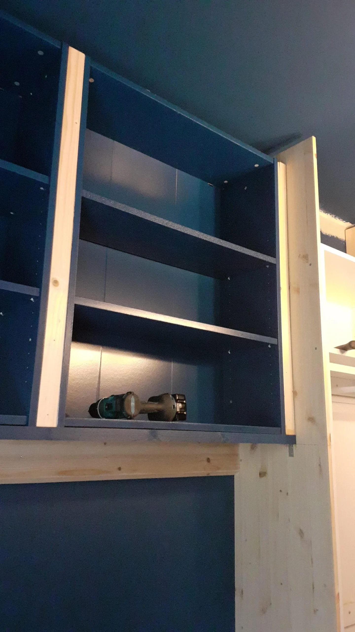 Vani libreria verniciati di blu appoggiati su una trave in pino durante il montaggio