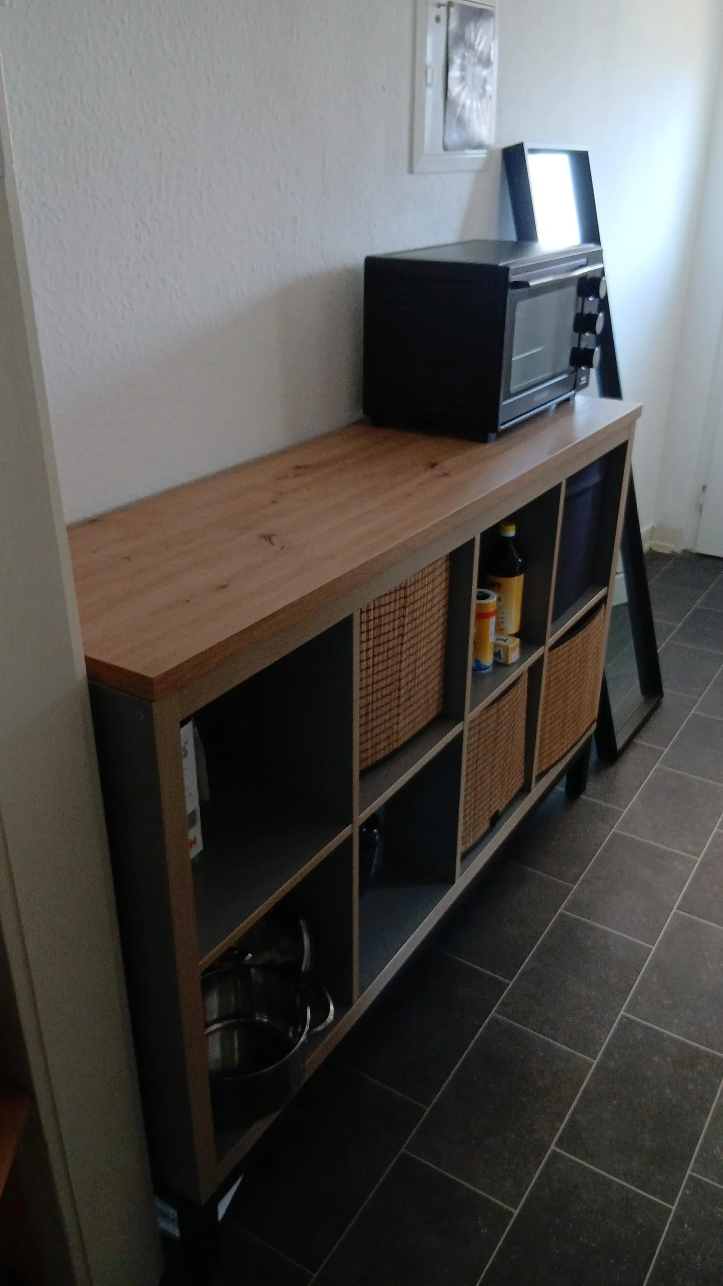 Credenza KALLAX rialzata su gambe con piano in legno, fornetto elettrico e cesti nei moduli aperti