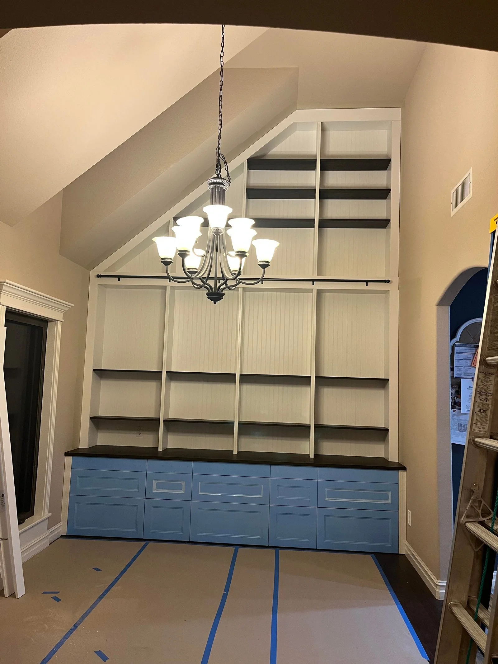 Parete libreria completata e verniciata di bianco, con binario nero della scala e cassetti blu